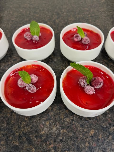 White ramekins with glossy red topping, small berry-like garnishes and green leaves.