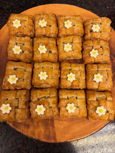 A wooden serving board of square golden pastries with small white flower decorations.