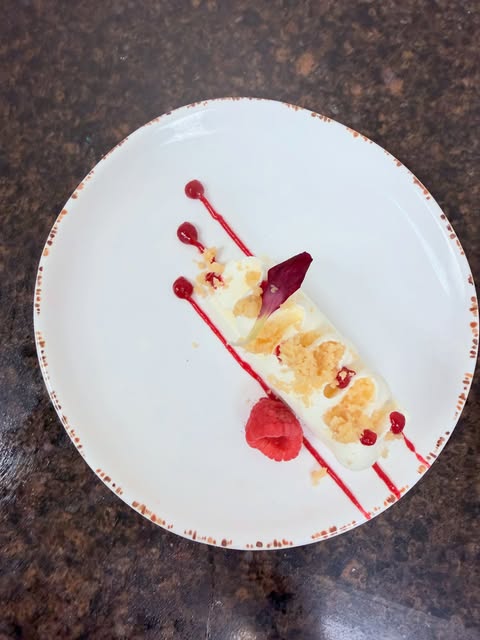 Individual plated dessert on a white plate, with red sauce lines, red garnish and a long pale central composition.